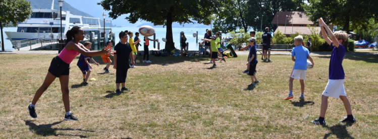 Kinder spielen Rugby auf einer Wiese an einem sonnigen Tag.