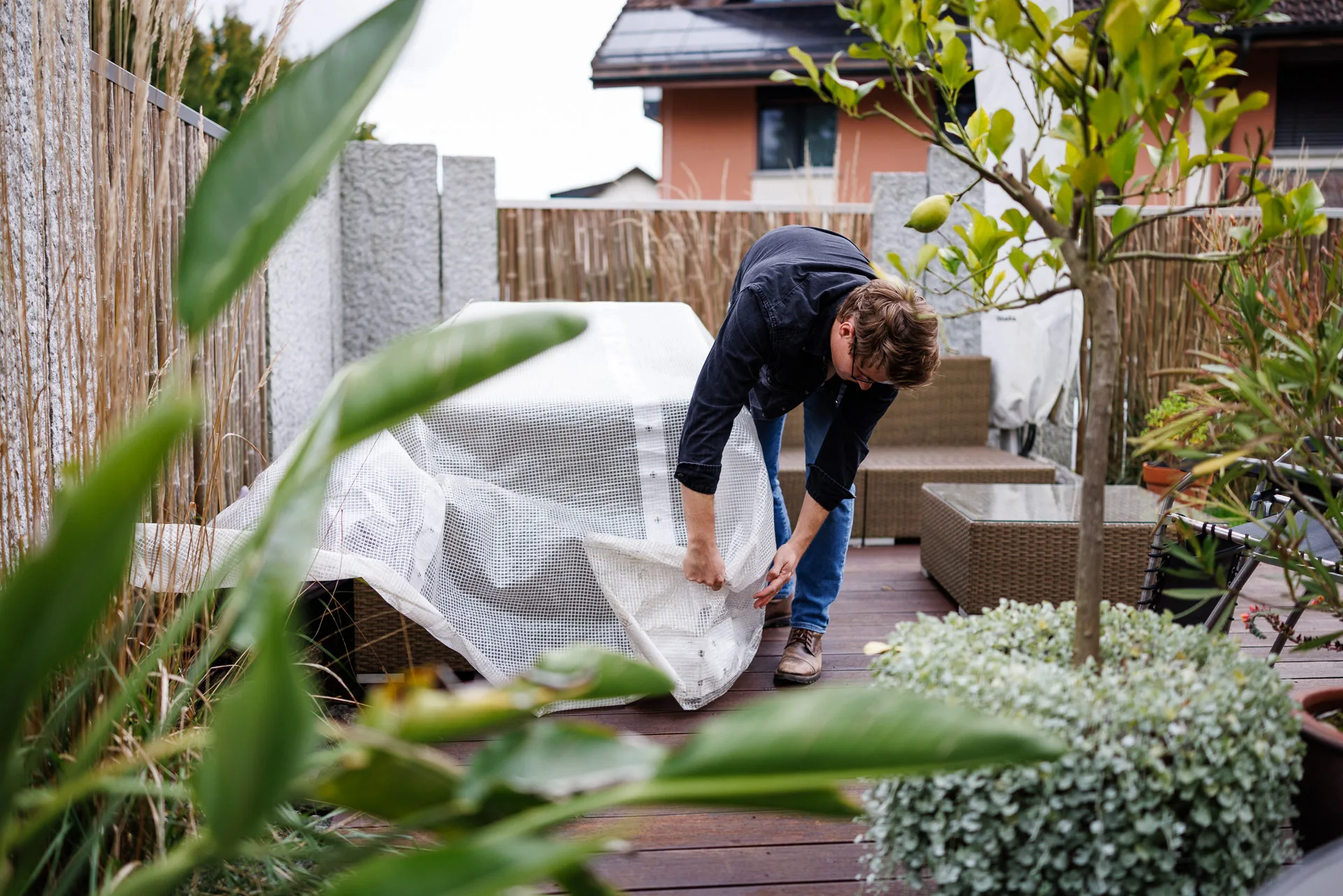 Ein Mann zieht eine Abdeckplane über seine Gartenlounge