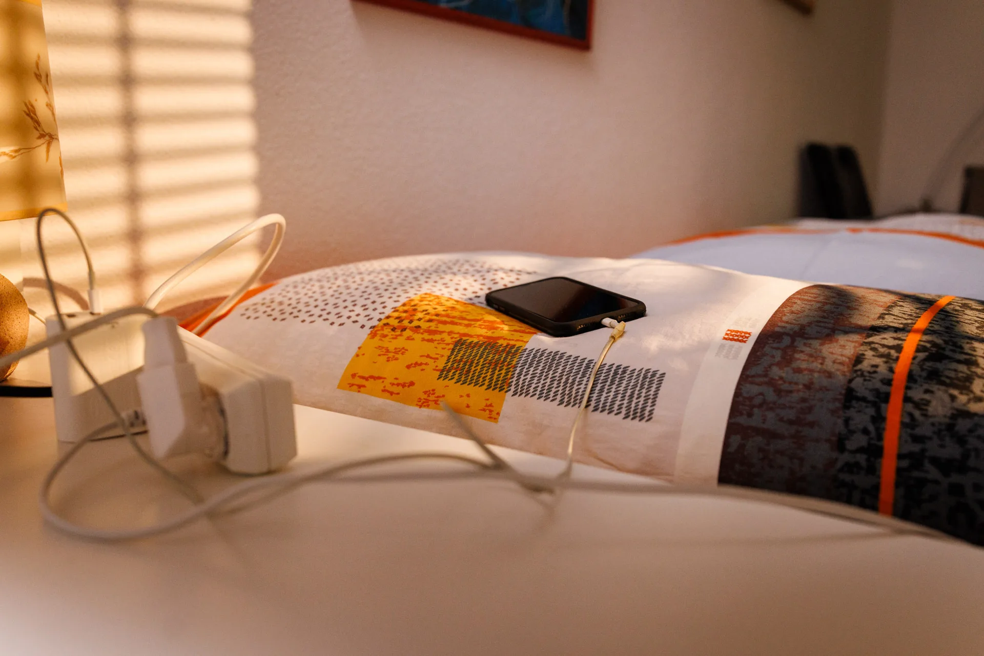 Ein Handy, eingesteckt zum aufladen, liegt auf dem Bett