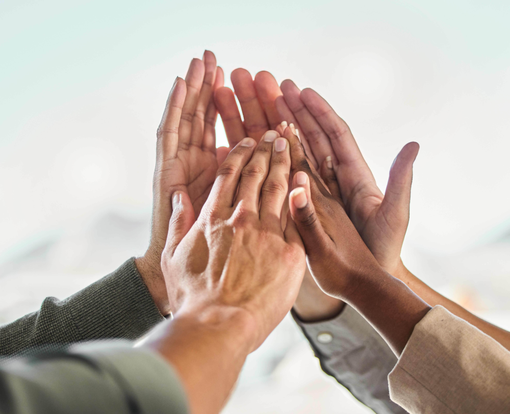 Nahaufnahme mehrerer Hände unterschiedlicher Menschen, die in einer High-Five-Geste oder einem gemeinsamen Handauflegen übereinandergelegt sind. Das Bild illustriert erfolgreiche Teamarbeit, gemeinschaftliches Handeln und den Zusammenhalt in der Gruppe. Es symbolisiert Kooperation, gegenseitige Unterstützung und die Kraft der Gemeinschaft in der Beratung, Therapie oder innerhalb einer starken Familiendynamik.