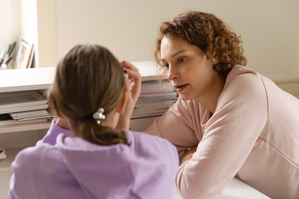 Nahaufnahme einer intensiven Beratungssituation: Eine Beraterin mit lockigem Haar blickt einer jungen Person in einem lila Hoodie tief und einfühlsam in die Augen. Die junge Person hält sich die Hand an die Stirn, was auf Stress, Überforderung oder tiefe Trauer hindeutet. Das Bild illustriert professionelle psychosoziale Hilfe, die Krisenberatung für Jugendliche und den geschützten Raum für emotionale Entlastung. Es symbolisiert Empathie, das Ernstnehmen von Sorgen und die Arbeit des Psychosozialen Gesundheitszentrums als erste Anlaufstelle bei psychischen Belastungen und Lebenskrisen.