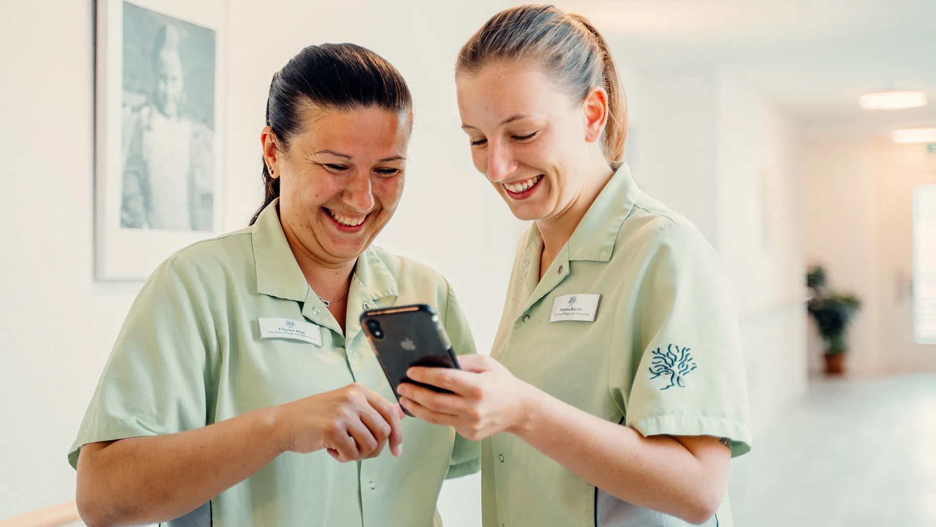 Zwei Mitarbeiterinnen des Alterszentrum Eiche stehen lachend beisammen und blicken gemeinsam auf ein Smartphone, aufgenommen 2021