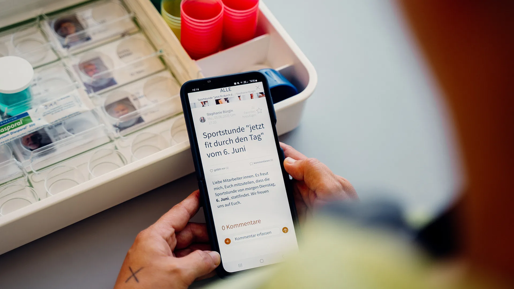 Smartphone wird mit beiden Händen gehalten; auf dem Bildschirm ist die geöffnete Mitarbeitenden-App der Jetzt Niedersimmental zu sehen, Aufnahme 2023.