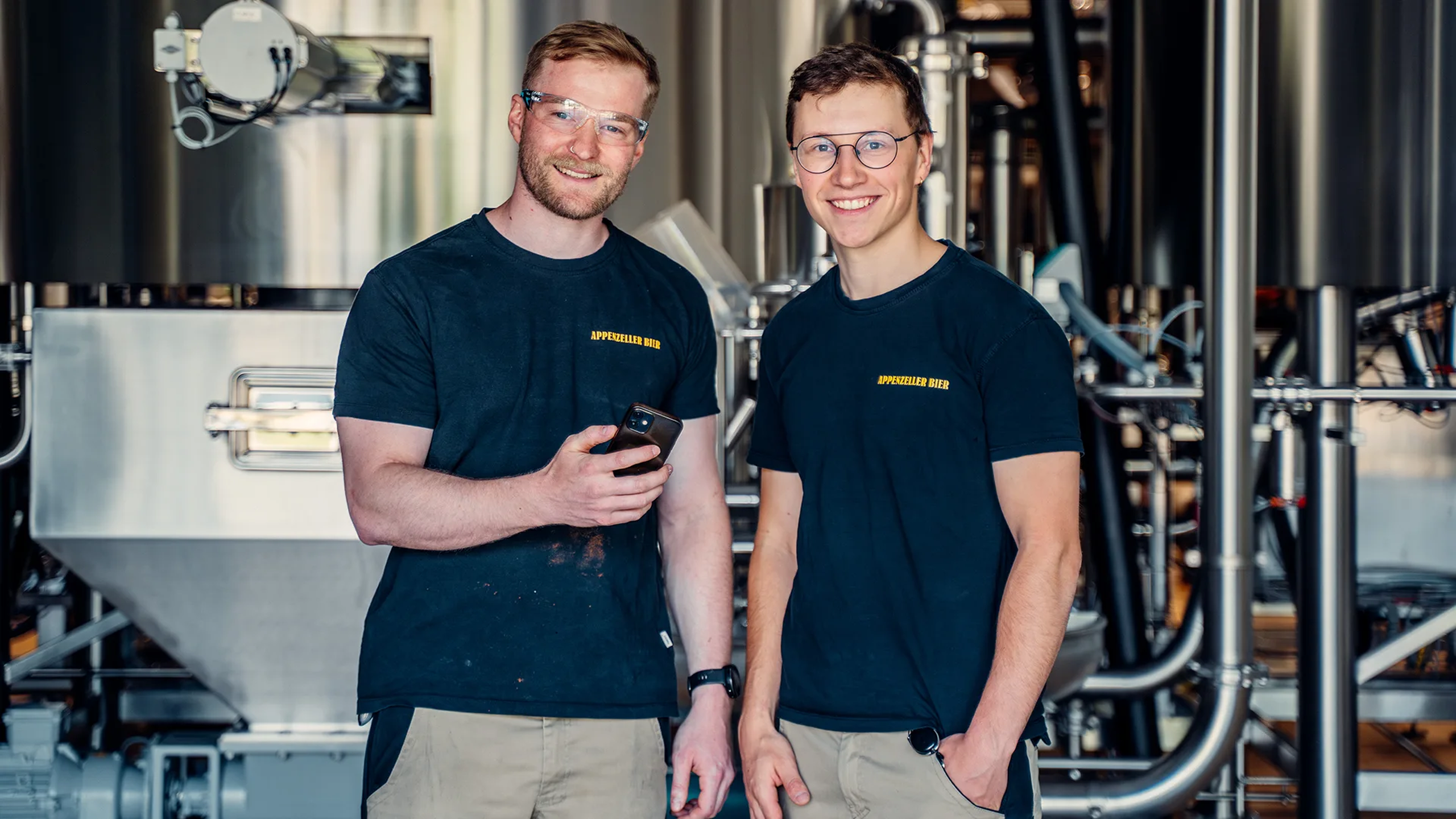 Zwei Mitarbeiter der Firma Appenzeller Bier nutzen die Mitarbeiter-App von Involve zur internen Kommunikation im Unternehmen, aufgenommen 2023