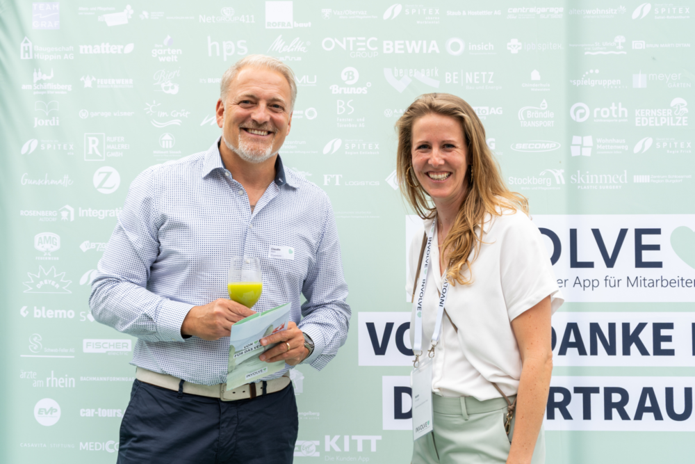 Helen Habegger, Gebietsverkaufsleiterin West, mit einem Kunden bei der Involve Night 2025. Sie stehen vor der Kundenlogowand und lächeln in die Kamera.