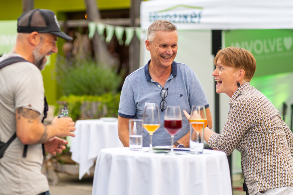 Zwei Kunden und eine Kundin stehen lachend an einem Stehtisch an der Involve Night 2025 im Burgrain Alberswil.