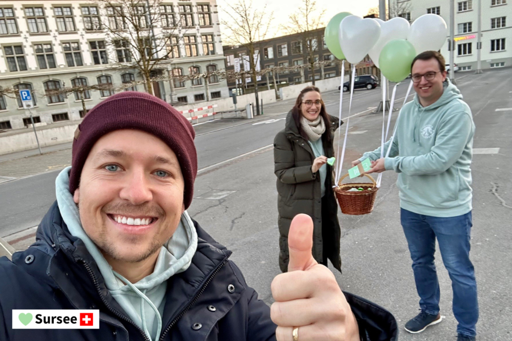 Drei lachende Mitarbeitende der Involve AG bei einer Wertschätzungsaktion in Sursee mit einem mit Ballonen geschmückten Korb.