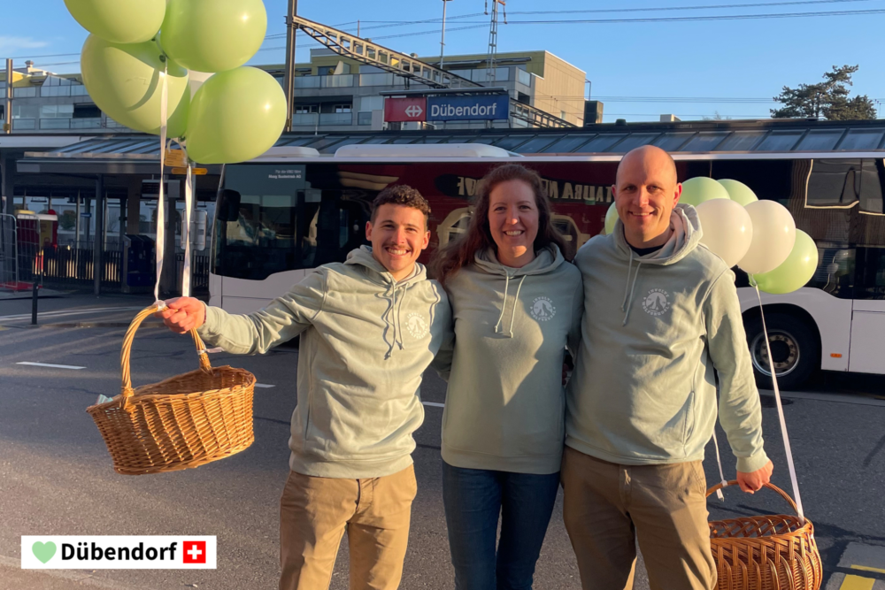 Drei Mitarbeitende der Involve AG stehen lächelnd beisammen. Zwei davon halten einen Korb mit Luftballonen in der Hand.