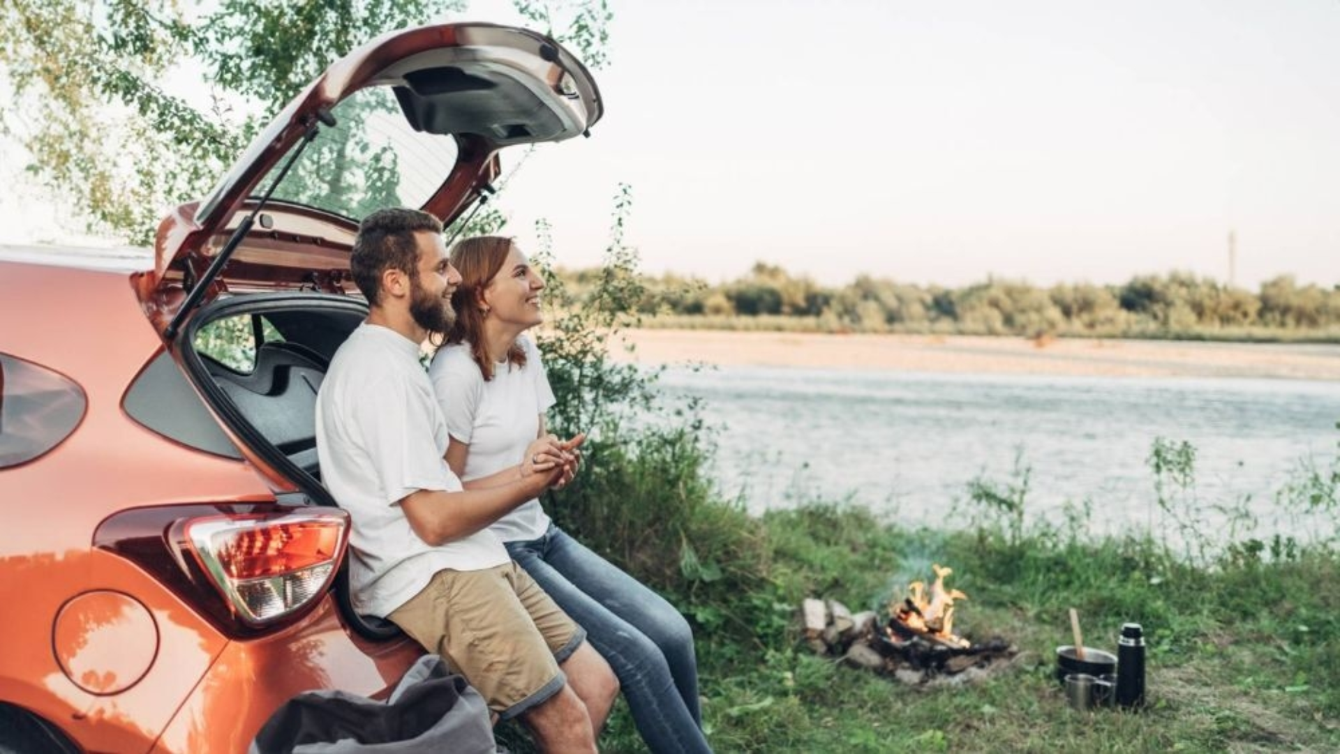 Ein Mann und eine Frau sitzen im Kofferraum eines Autos am See.