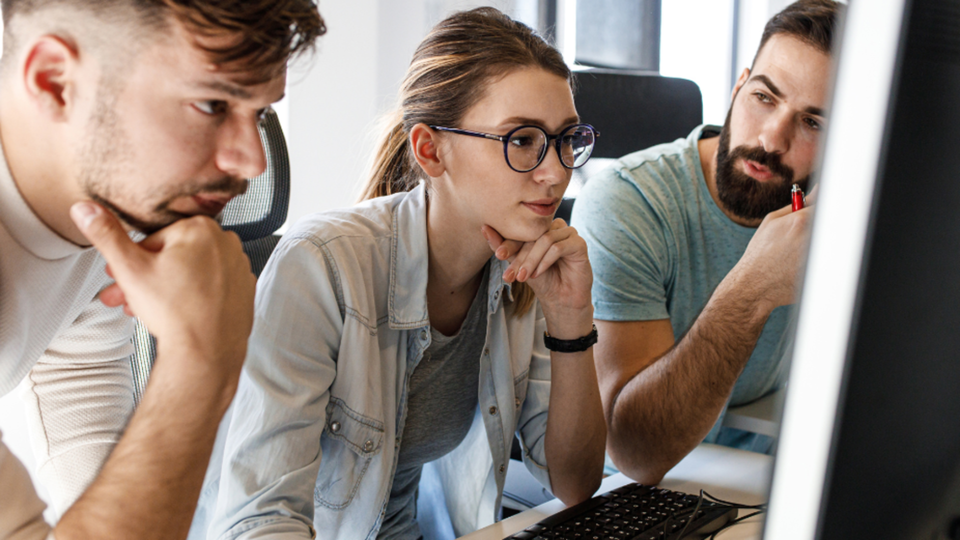 Drei Personen schauen sich etwas auf einem Bildschirm an und besprechen es.