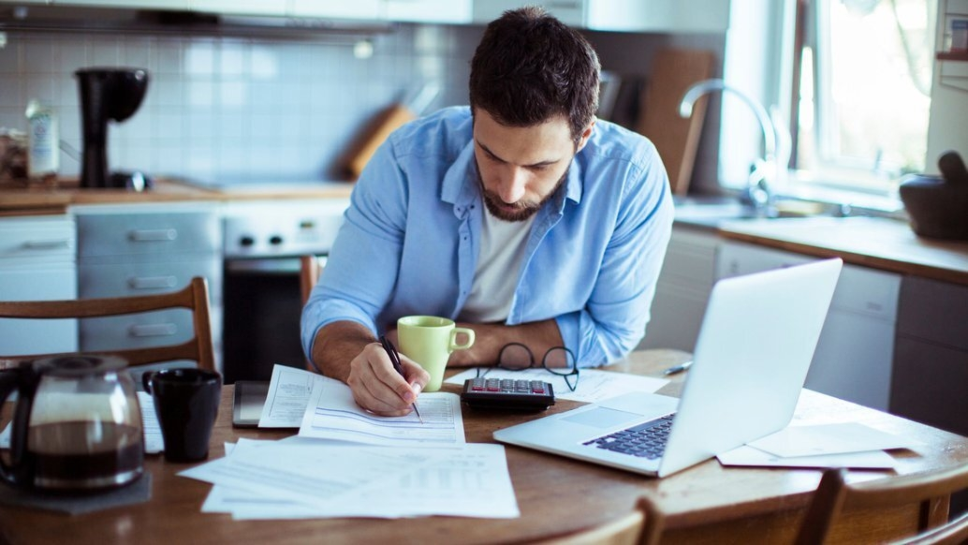 Mann an einem Tisch, der an seinem Laptop Rechnungen bezahlt.