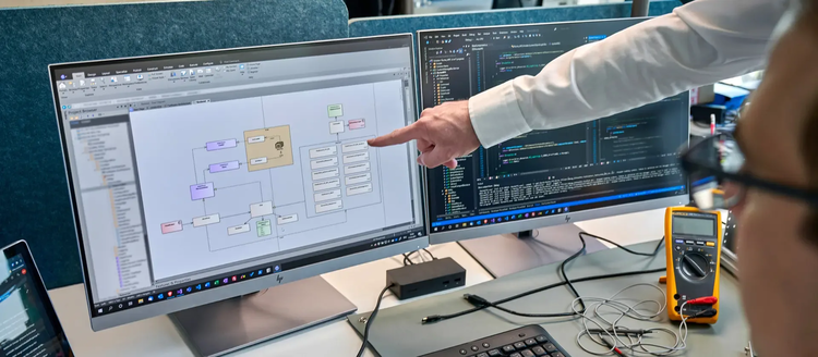 Zwei Mitarbeitende sitzen vor dem Computer und tauschen sich aus.