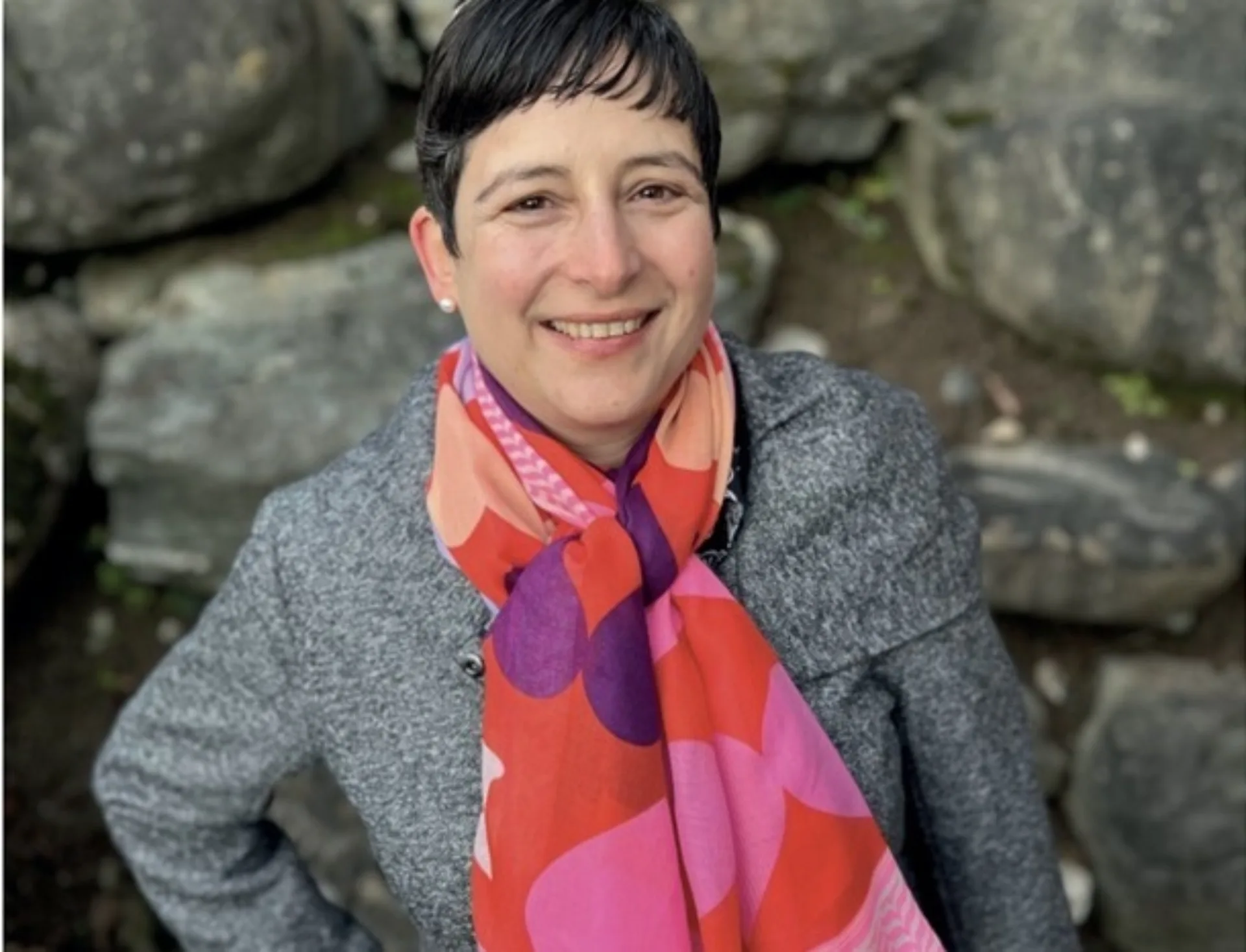 Lachende Frau mit kurzen, schwarzen Haaren vor einer Natursteinwand