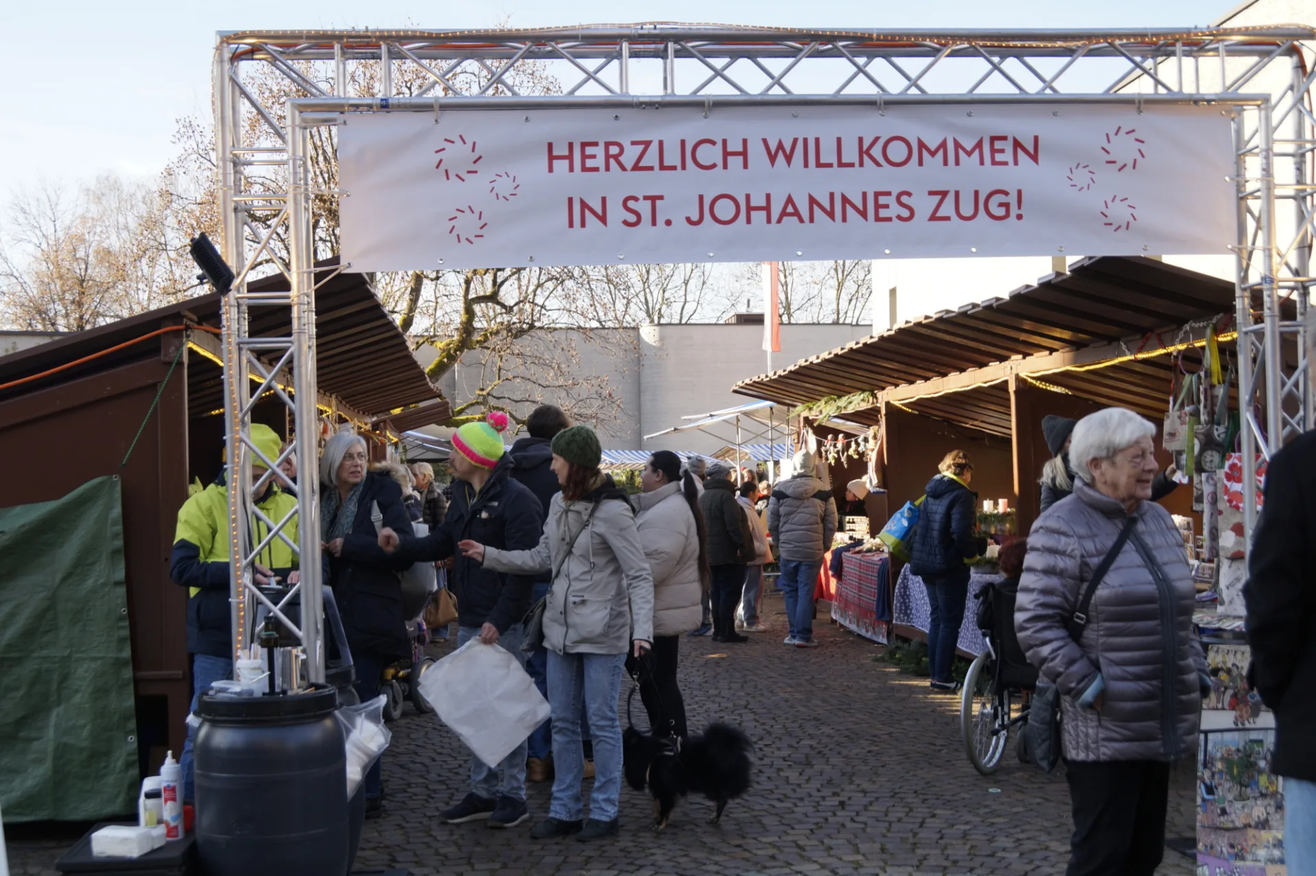 Menschen drängen unter dem Tor mit dem Schriftzug Willkommen in St. Johannes zwischen die Marktstandreihen