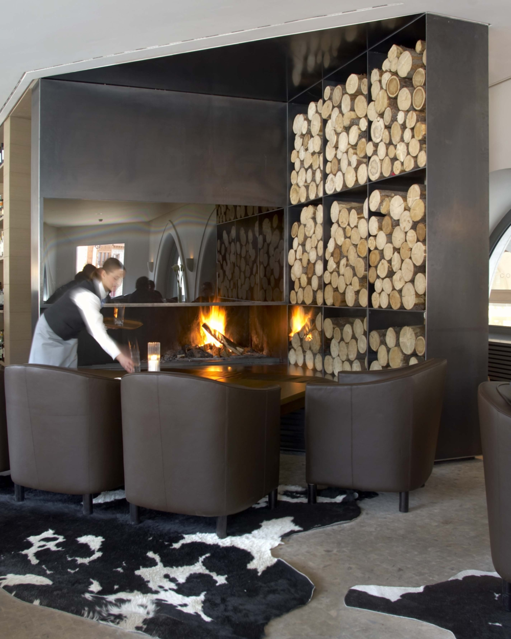 Offenes Designcheminée aus rohem Stahl mit Nische zur Aufbewahrung von Holzscheiten.