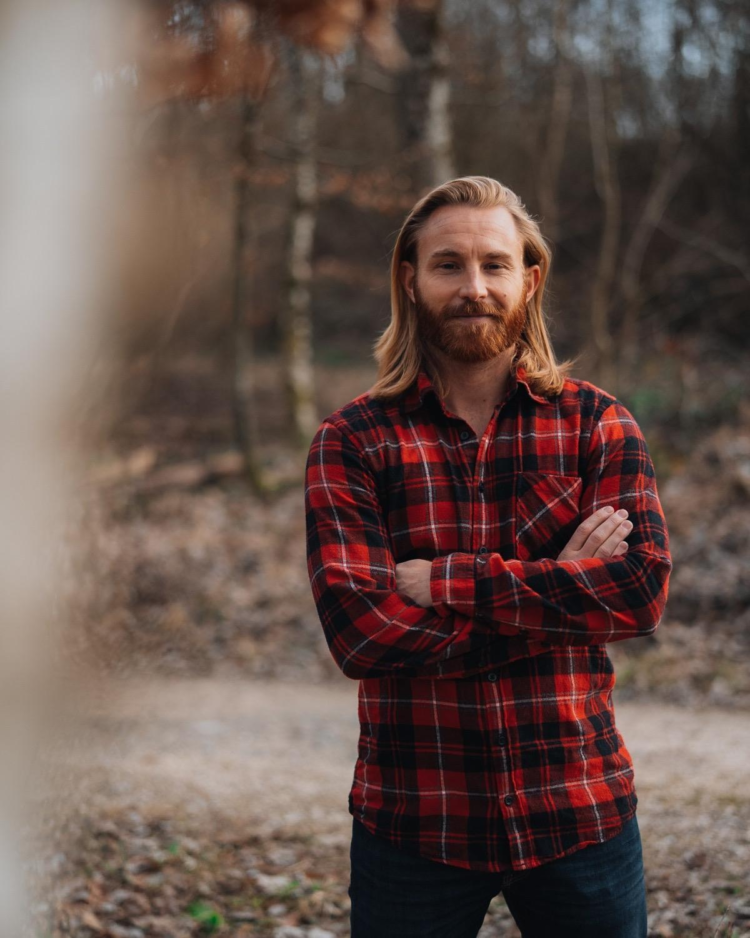 Portrait von Michael Weber, ein Mann mit langen dunkelblonden Haaren und rotem Holzfällerhemd