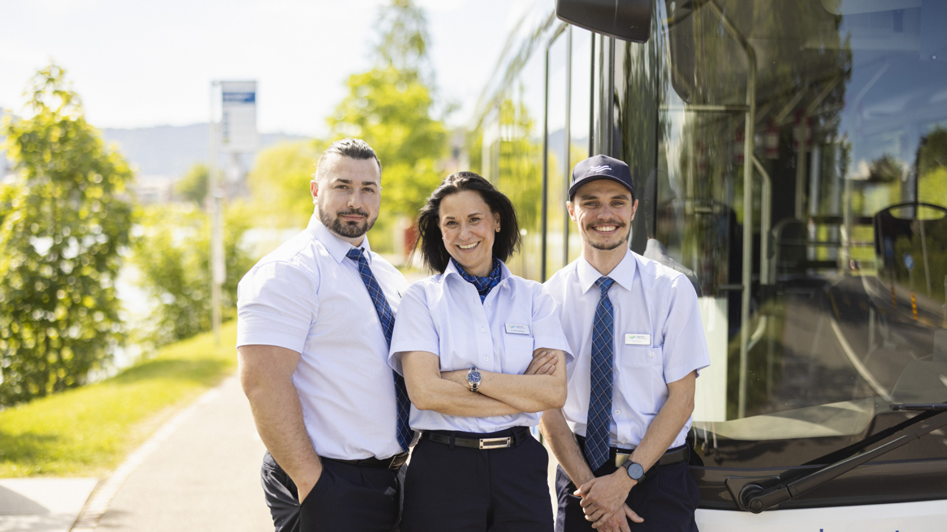 Drei Personen in Busfahreruniform stehen vor Bus